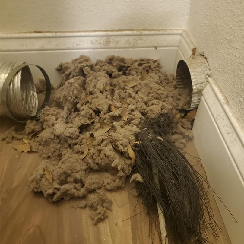 Material removed from a duct system piled on the floor beside the open duct