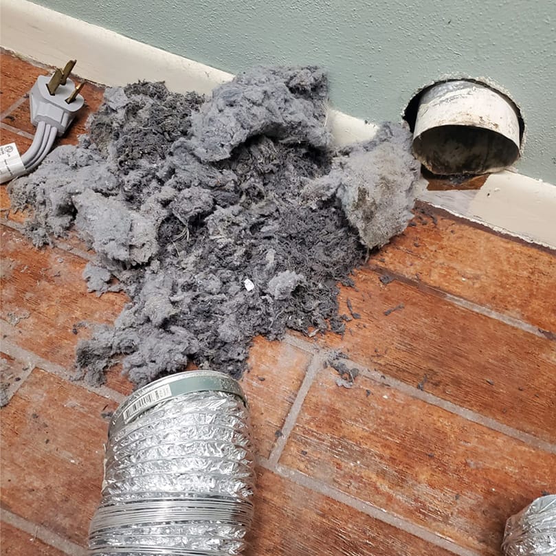 Lint removed from a dryer duct on the floor beside the disconnected duct