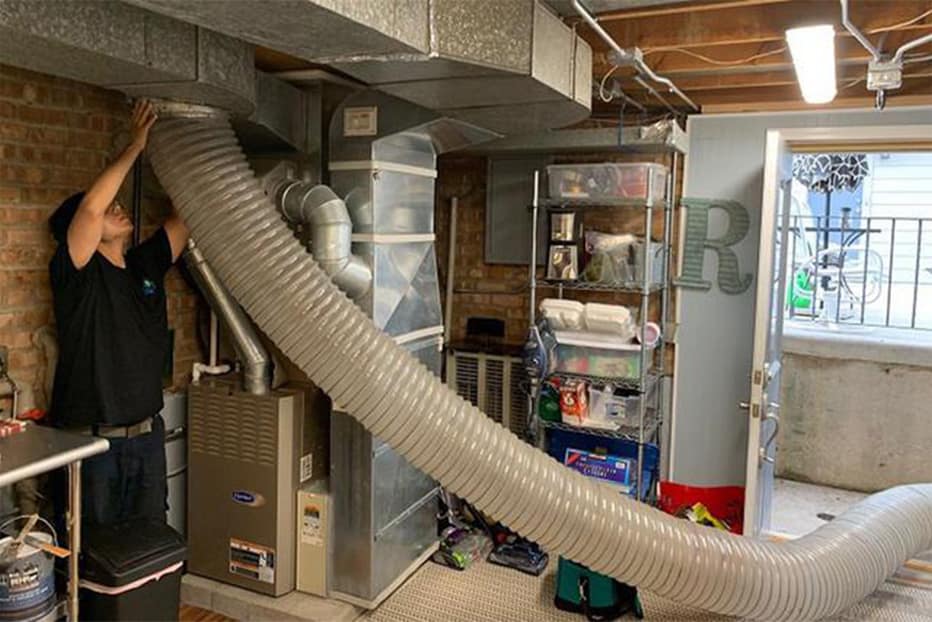 Technician routing a duct cleaning hose to a basement furnace